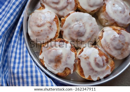 Cinnamon buns sit on a blue and white checked towel, straight from the oven. An icing glaze tops them.