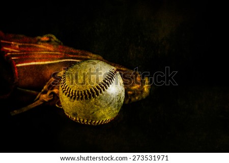 A rustic looking baseball sits in front of a glove - grunge background and detail.