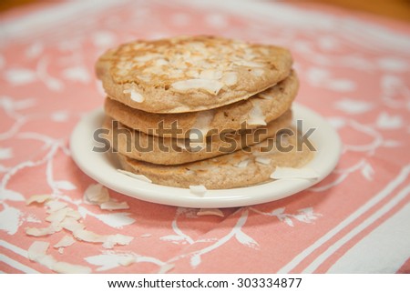 A stack of whole grain coconut pancakes sits on a small white plate with a peach and white napkin beneath.