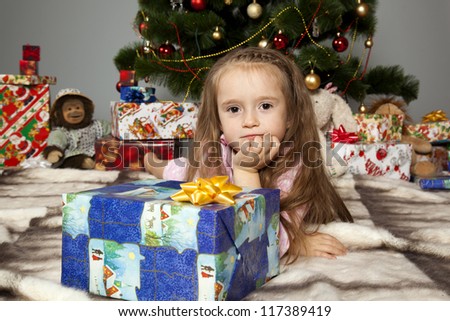 Girl in pajamas lying under the Christmas tree with gift in hand