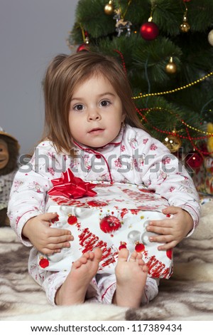 Girl in pajamas sitting under the Christmas tree with gift in hand