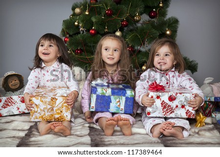 Three girls in pajamas sitting under the Christmas tree with gifts in their hands