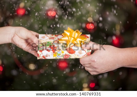 Gift delivery  between a man and a woman under snowfall in front of Cristmas tree