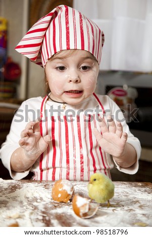 little chef in the kitchen ,wearing an apron and headscarf,surprise looking at hatched chick