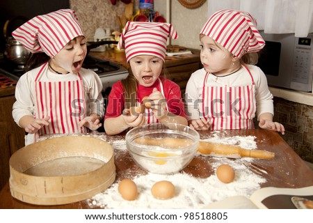 Three little chefs enjoying in the kitchen making big mess. Little girls making bread in the kitchen
