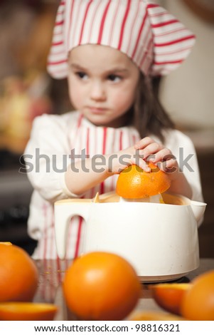 Little girl making fresh and healthy orange juice with kitchen appliance