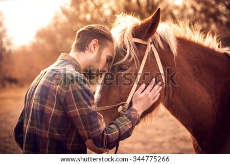 Young man hugs a horse. Autumn outdoors scene