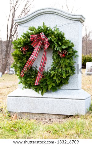 A large wreath is tied to a monument in a cemetery at Christmas time.