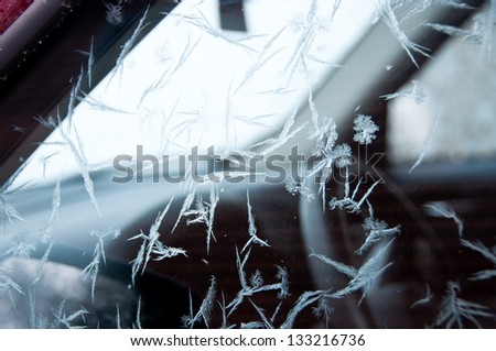 Frost crystals cover the surface of the driver's side window of a car.
