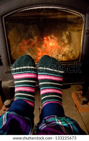 A pair of feet in thick striped socks are shown in front of a wood stove.