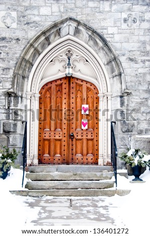 A stone church with an ornate wooden door has hearts hung to one side.