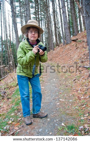 A photographer stares intently at the camera while hiking on a trail.