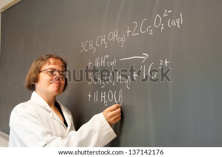A woman chemistry instructor writes out a chemical equation on a chalk board. The equation describes the chemistry behind the \