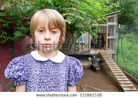 A young girl with a sullen expression stands in a turkey pen.