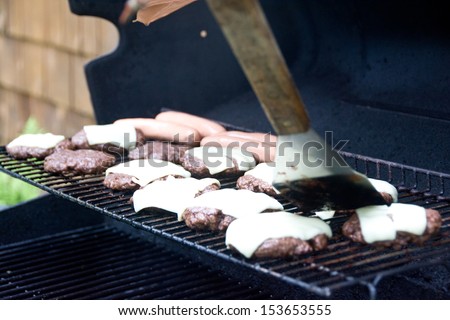 A spatula is being used to move home made cheeseburgers on a backyard grill.