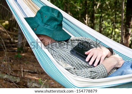 A relaxed man sleeps in a hammock with tablet.
