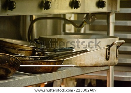 Large, well-used cooking pots are stored in a rack under the cooking range in a commercial kitchen.