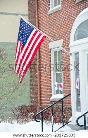 A US flag flies outside an office building with heavy snow falling.