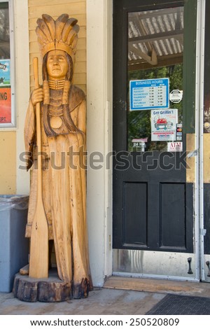 Marshfield, VT, USA - May 18, 2014: A sign on the door announces business hours while a carved Indian stares quietly into space on the porch of the Marshfield Village Store on a quiet afternoon.