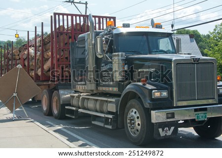 Plainfield, VT, USA - July 21, 2014: A double trailer logging truck slows down as it passes through the center of downtown Plainfield on this sunny summer morning.