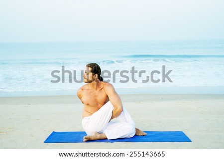 Long Hair Athletic Man with No Shirt doing Yoga on Blue Mat at the Beach\
Seated Spinal Twist posture â?? Ardha Matsyendrasana