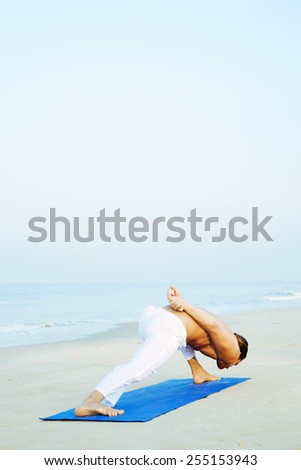 Long Hair Athletic Man with No Shirt doing Yoga on Blue Mat at the Beach
