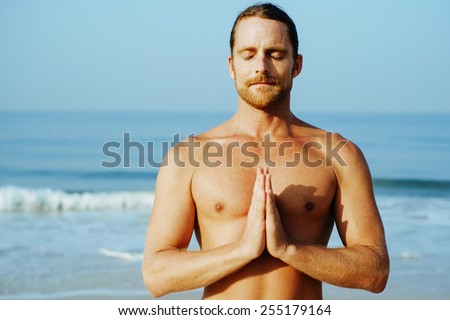 NAMASTE\
Long Hair Athletic Man with No Shirt doing Yoga on Blue Mat at the Beach