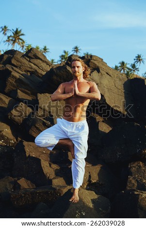Long Hair Athletic Man with No Shirt doing Yoga on the Rocks