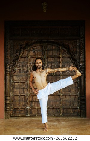Indian ethnicity young man wit a strong body showing Extended Hand To Big Toe yoga pose (Utthita Hasta Padangustana) in front of old oriental style door.