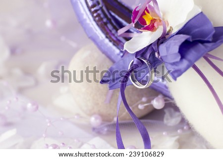 Some decorative stuff like wedding ring, ribbons, flower and string of beads all in violet and white.
