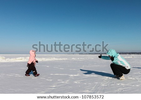Mother and baby girl play on snow near the sea