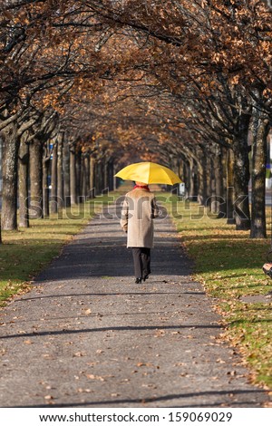 Elderly woman in the fall park with yellow umbrella