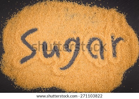 word sugar written in brown granulated sugar on dark stone background