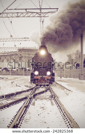 Retro steam train departs from the railway station at sunset. Vintage image.