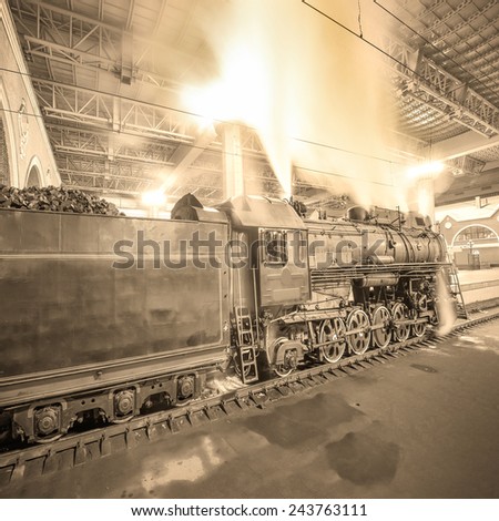 Steam train arrives to the station at night time. Vintage image.