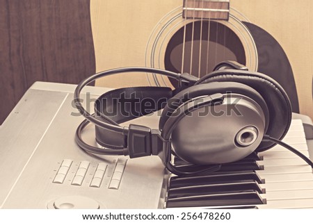 Digital midi keyboard, headphones and acoustic guitar in the studio.