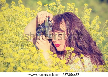Woman shooting flowers on the meadow with vintage photo camera.