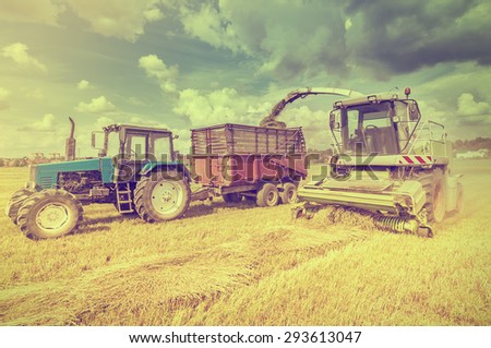Agriculture machines collect hay in the field in a summer day.