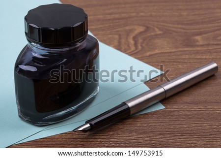 An inkwell, sheets of paper and a fountain pen on wooden texture imitating a desk.