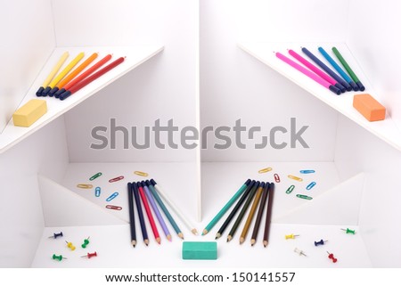 Multicolored pencils, pins and erasers on a white construction.