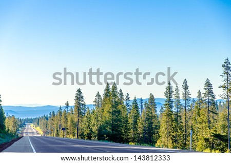 Long scenic highway passing through a lush green forest with blue hills in the background near Bend, Oregon