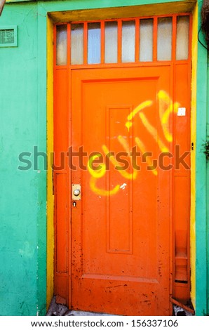An orange door with graffiti scrawled on it in La Boca neighborhood in Buenos Aires, Argentina