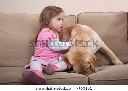 A young girl with Down Syndrome sitting on a couch with a puppy. A form of therapy.