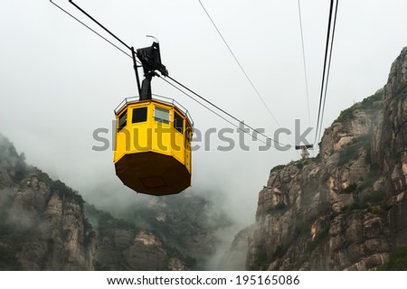 Photo of yellow cable car taken during autumn foggy day. Fog and Monserrat hill in background