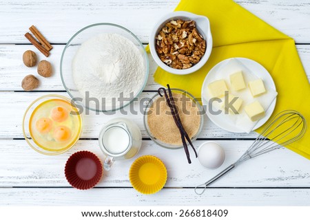 Baking cake in rural kitchen - dough recipe ingredients (eggs, flour, milk, butter, sugar) with yellow napkin on white wooden table from above.