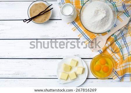Baking cake in rural kitchen - dough recipe ingredients (eggs, flour, milk, butter, sugar) on white wooden table from above.