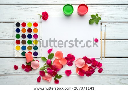 Desk of creative worker. Paints, brush, paper, rose petals and leaves. Top view background.