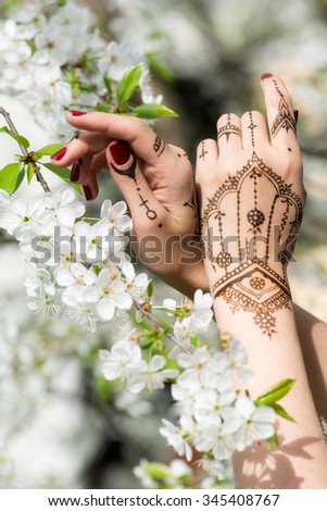 Red manicured hands with Mehndi in spring cherry blossom, Indian tradition. Vertical composition.