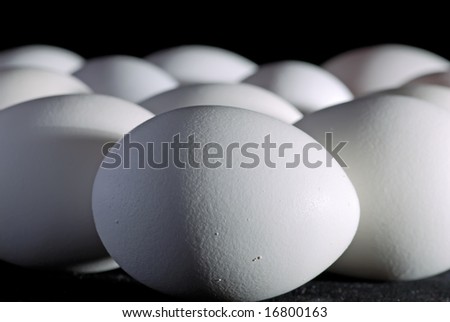 A lots of white chicken eggs on black background, close-up. Focus is on the egg at the front.