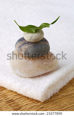 An image of a folded white bath towel and three stones balanced on each other with green leaf